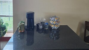 Una encimera de cocina con una cafetera, una taza, una jarra de vidrio y un dispensador de cápsulas de café.