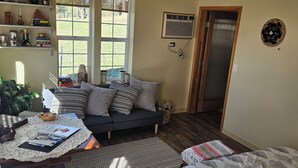 Una habitación acogedora con un sofá, una mesa con papeles, una estantería y una puerta que da a otra habitación.