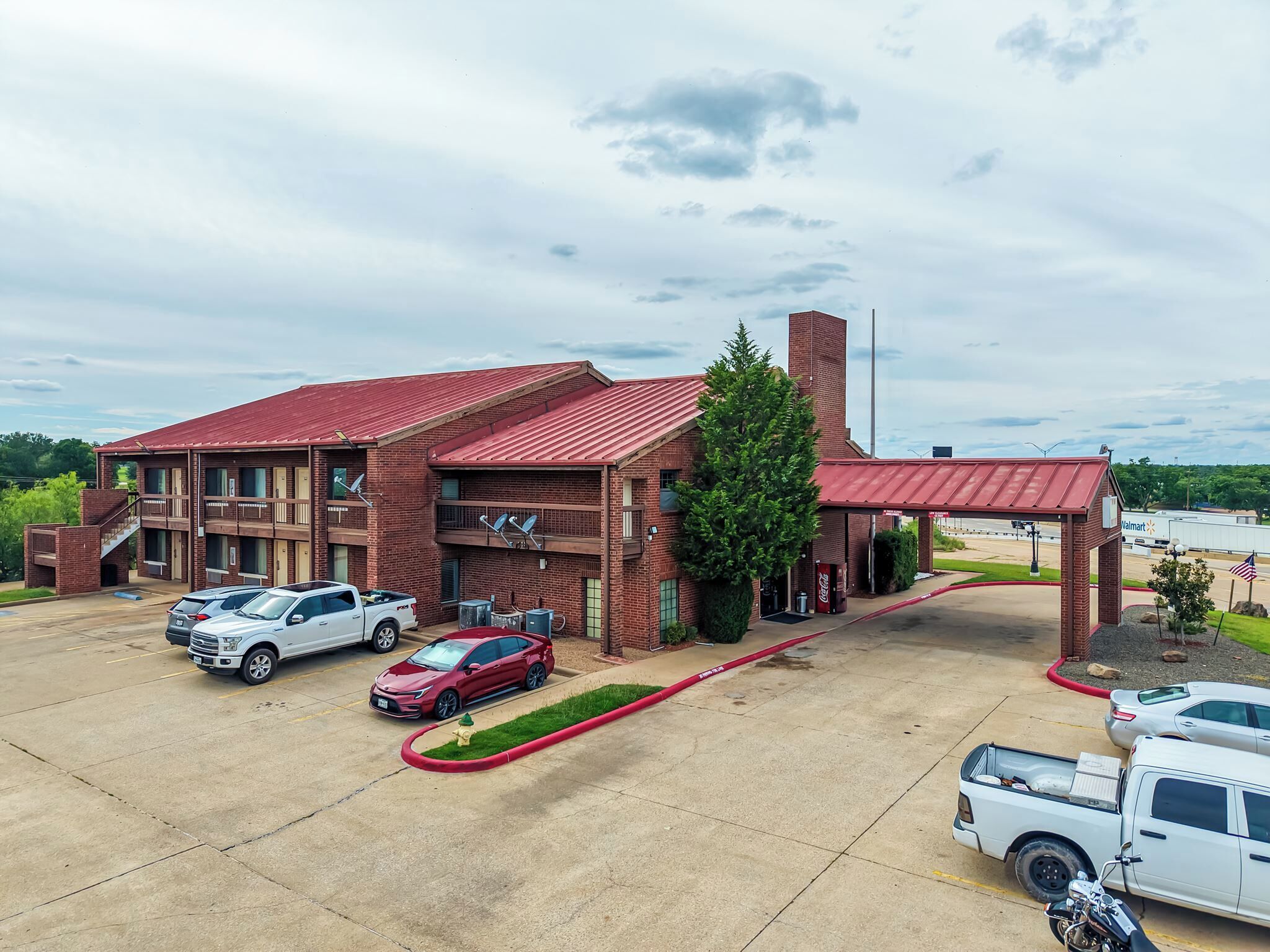 A motel with a red roof, multiple parking spaces, and a Walmart sign in the background.