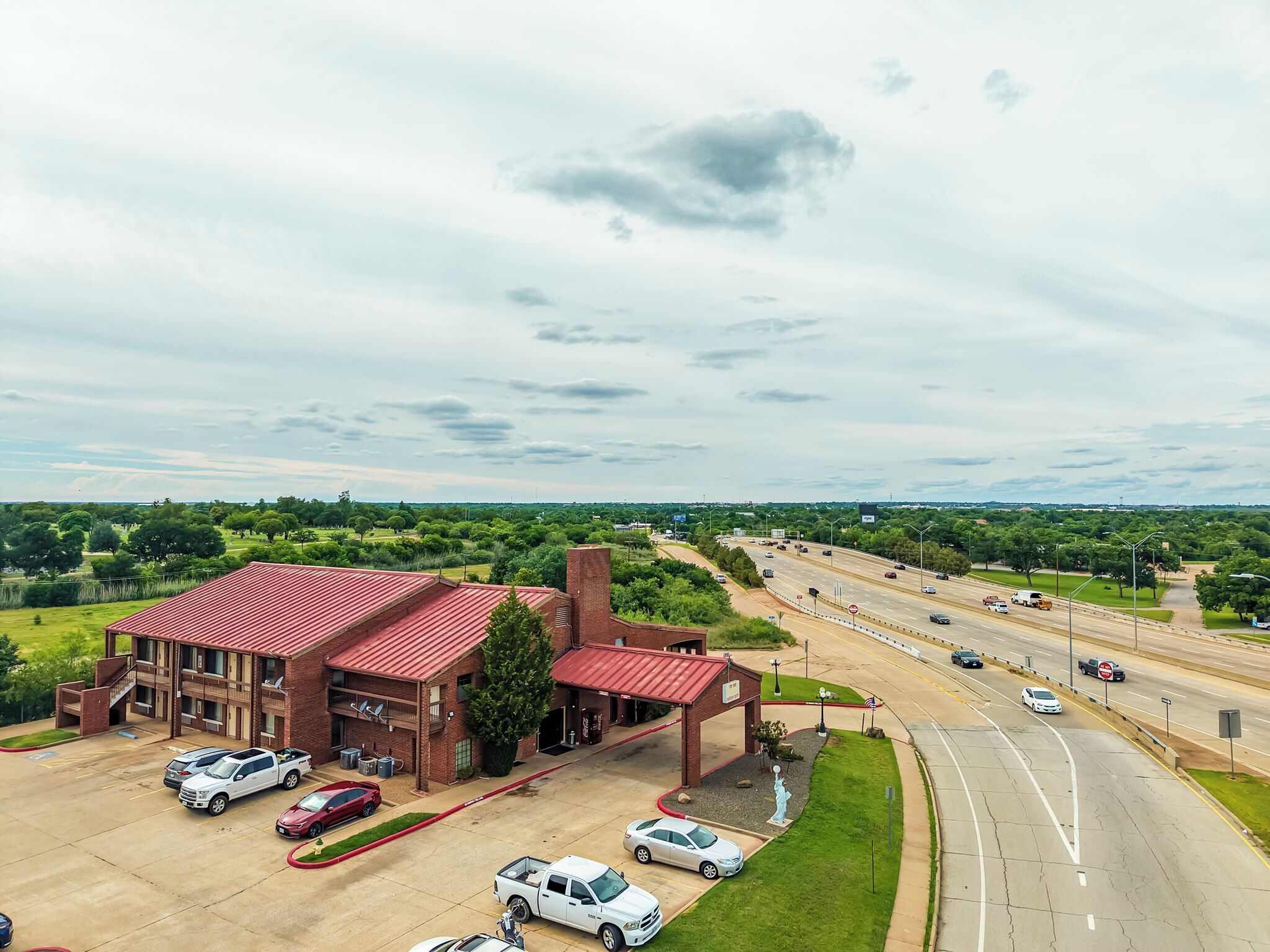 A multi-story building with a red roof, parking lot, and a highway in the background.