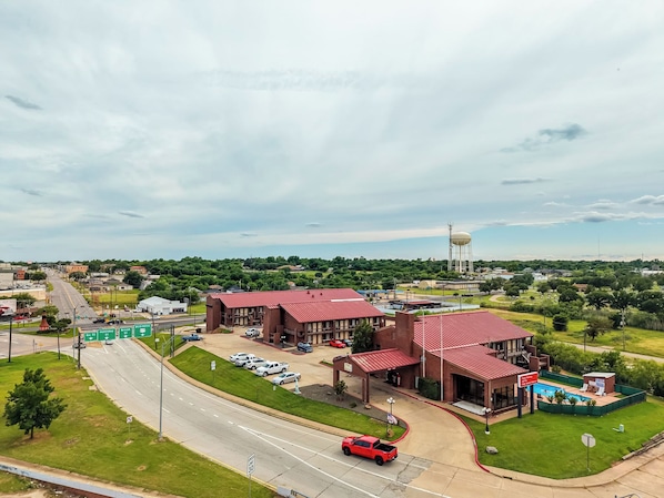 A multi-story hotel with a red roof, a swimming pool, and a parking lot.