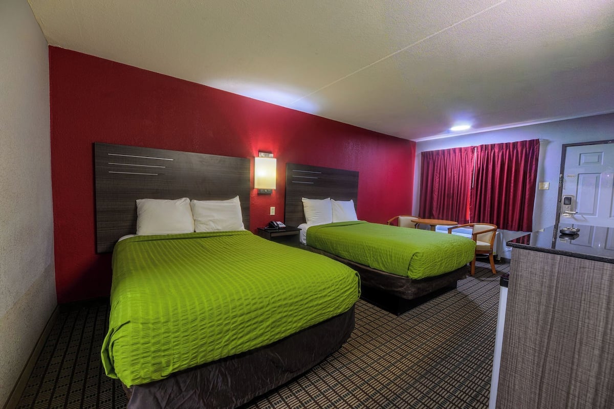 Habitación de hotel con dos camas, un escritorio, una silla y una cortina roja.