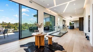 A modern interior with a large glass door leading to a balcony, a round wooden table, and a leather rug. - Casa Adriana by Oraklus (Pacific Palisades)