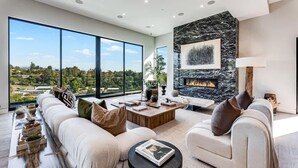 A modern living room with a large sofa, a coffee table, and a fireplace. - Casa Adriana by Oraklus (Pacific Palisades)