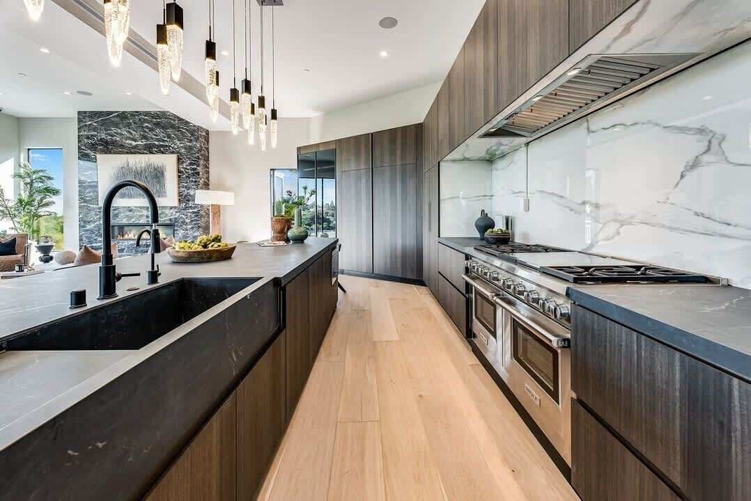 Una cocina moderna con una isla central, armarios oscuros, un salpicadero de mármol e iluminación colgante.