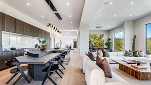 A modern kitchen with a central island, dining area, and a living room with a sofa and coffee table. - Casa Adriana by Oraklus (Pacific Palisades)