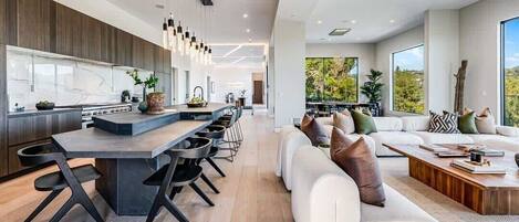 A modern kitchen with a central island, dining area, and a living room with a sofa and coffee table.