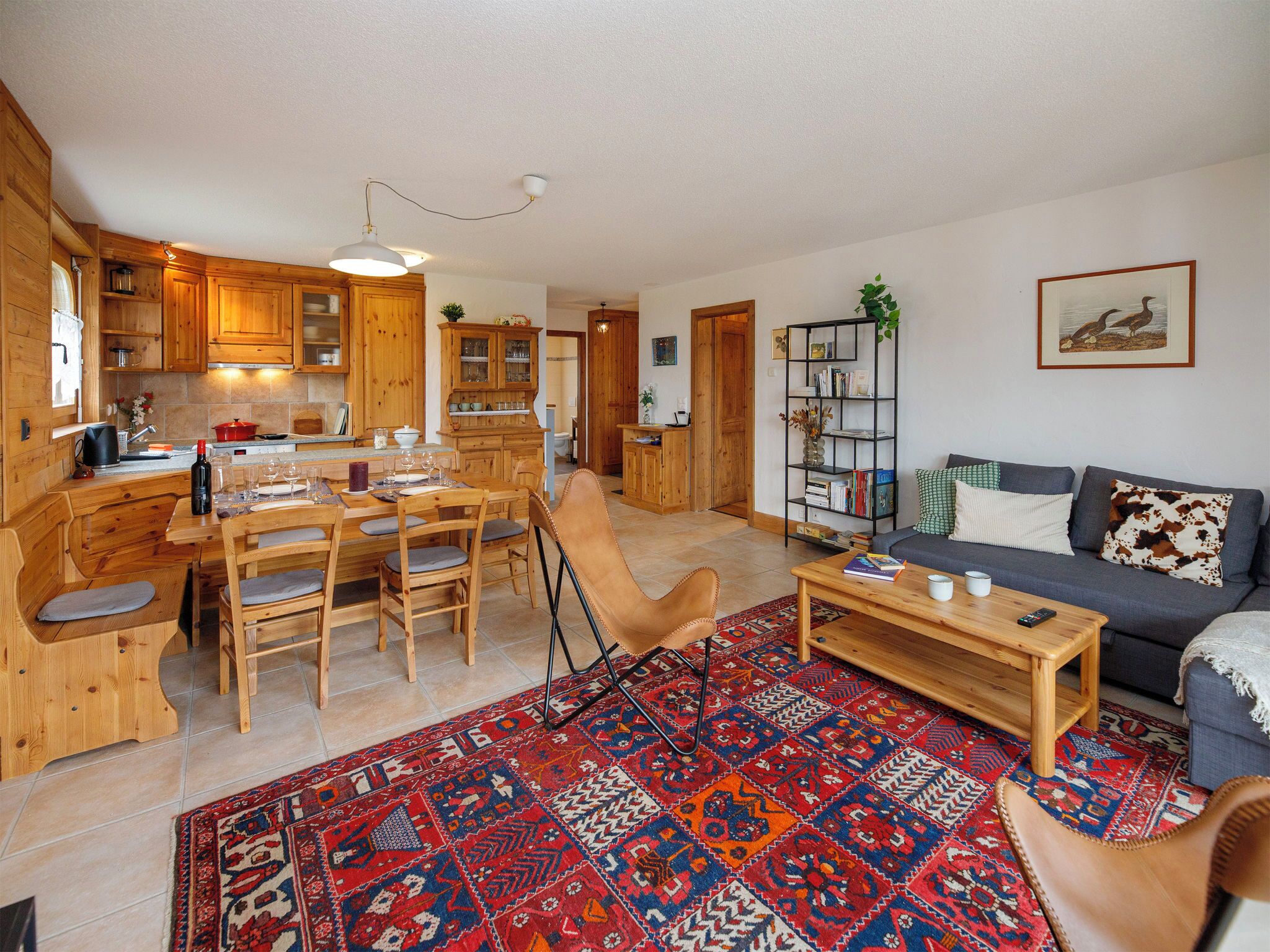 A cozy cabin interior with wooden furniture, a dining area, a living room with a sofa, and a bookshelf.