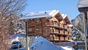 Un chalet en bois doté de balcons, entouré d’arbres et de montagnes couverts de neige.