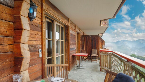 Une cabane en bois avec un balcon, une table et des chaises, et une vue sur la montagne.