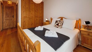 Une chambre à coucher avec un lit en bois, une table de chevet avec une lampe, une armoire et un luminaire suspendu.