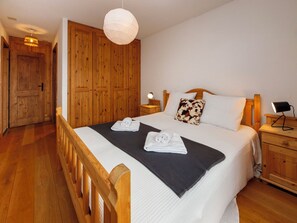 A bedroom with a wooden bed, a bedside table with a lamp, a wardrobe, and a hanging light fixture. - Ardève 5 by Interhome (Ovronnaz)