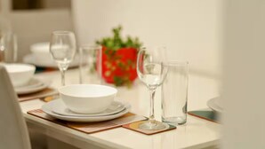 A dining table set with white plates, bowls, and clear glassware, with a red decorative bowl in the background. - Stylish 2BR Apartment Parking PS5 Wifi (Darwen)