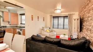 A compact living space with a kitchenette, a sofa, a dining area, and a stone wall. - Stylish 2BR Apartment Parking PS5 Wifi (Darwen)