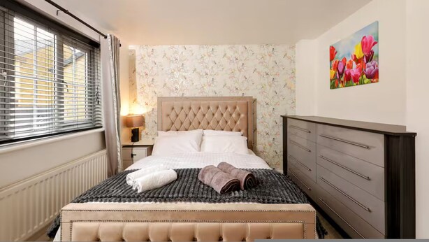 A bedroom with a bed, a dresser, a lamp, and a window with blinds. - Stylish 2BR Apartment Parking PS5 Wifi (Darwen)