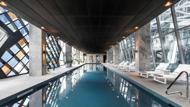 An indoor swimming pool with clear glass walls, lounge chairs, and a modern architectural design. - Sky High Views CBD Stay Near Ritz Carlton (Melbourne)