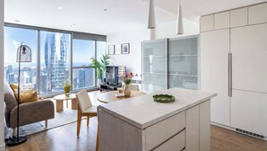 A modern kitchen with a large island, a dining area with a view, and a living room with a sofa and a TV. - Sky High Views CBD Stay Near Ritz Carlton (Melbourne)