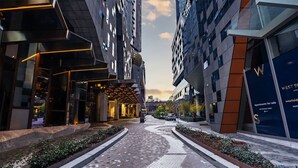 A modern building with a pathway leading to a building entrance, surrounded by greenery and other structures. - Sky High Views CBD Stay Near Ritz Carlton (Melbourne)