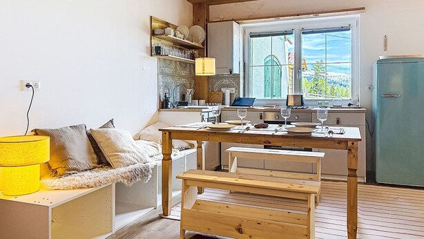 A compact kitchen with a wooden table, a bench, and a window with a view.