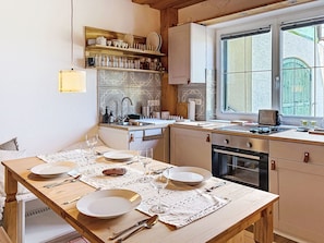 Una cocina con una mesa de comedor para cuatro personas, una ventana con vistas y una estantería empotrada con vajilla.