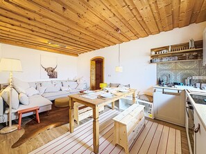 Una sala acogedora con techo de madera, un sofá, una mesa de comedor y una zona de cocina con estanterías.
