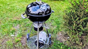A portable grill set up outdoors with a grassy field and trees in the background.