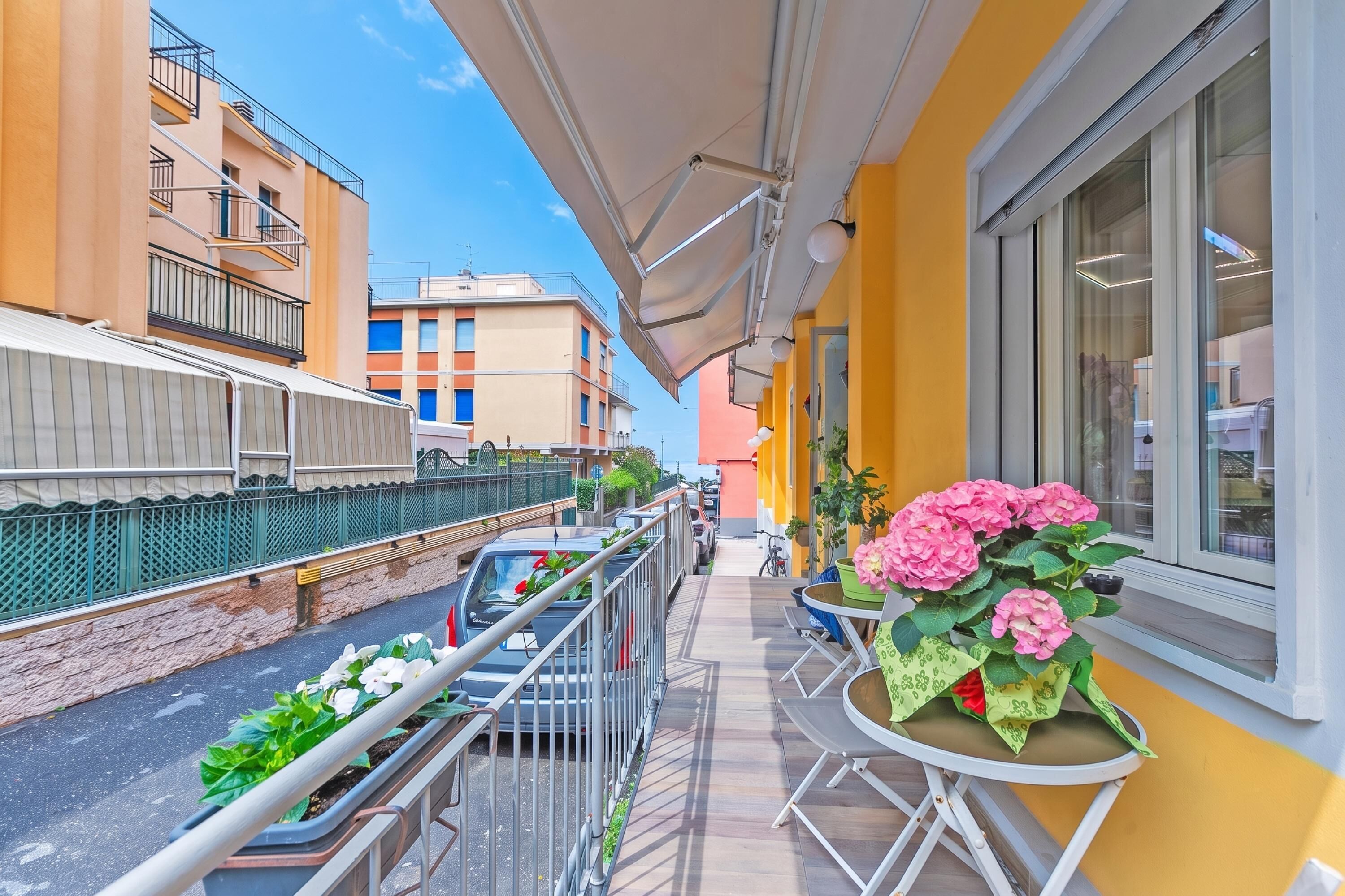 Un balcón con vistas a una calle estrecha, una mesa con flores y una barandilla.