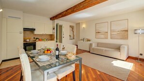 Una cocina moderna con vigas de madera, un comedor con mesa de vidrio y una sala de estar con sofá y obras de arte.