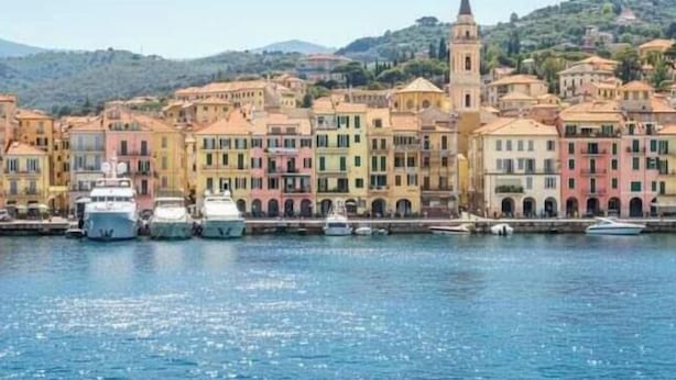 Une ville côtière aux bâtiments aux couleurs vives, dotée d’un port de plaisance et bordée d’une colline en arrière-plan.