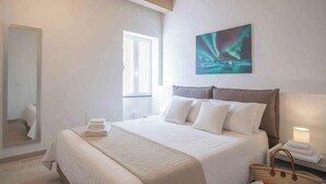 Une chambre à coucher avec un lit, des oreillers, une table de chevet, une lampe, un miroir et un tableau accroché au mur.