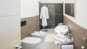 Un bagno moderno con bidet, due lavabi, cabina doccia in vetro e accappatoio su un appendiabiti.