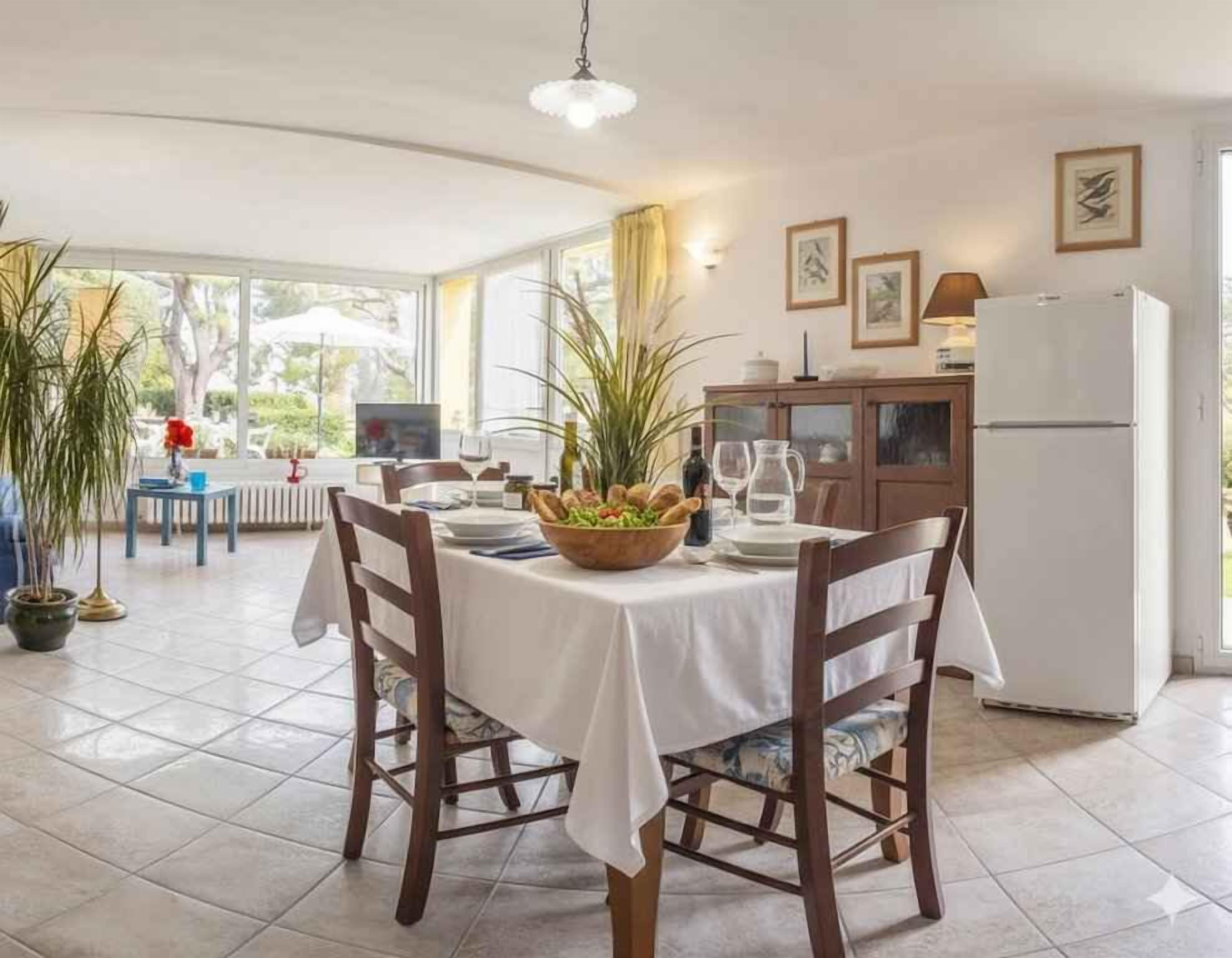 Un coin repas avec une table dressée pour deux personnes, entourée de chaises, et offrant une vue sur l’extérieur grâce à de grandes fenêtres.