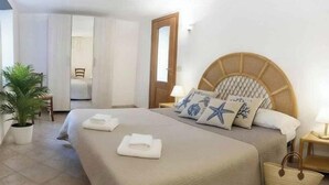 Ein Schlafzimmer mit einem Bett, einer Zimmerpflanze, einer Tür und einem Nachttisch mit einer Lampe.