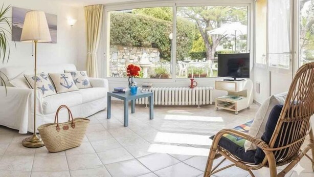 Ein Wohnzimmer mit einer Couch, einem Korbsessel, einem Fernseher und Blick ins Freie.