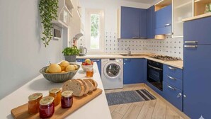 Une cuisine moderne avec des meubles bleus, un lave-linge et un plan de travail sur lequel on trouve du pain et des bocaux.