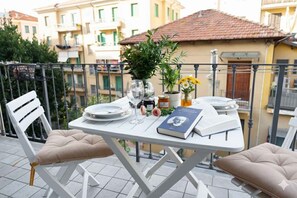 Ein Balkon mit Tisch, gedeckt für zwei Personen, mit Buch, Gläsern und Topfpflanzen.