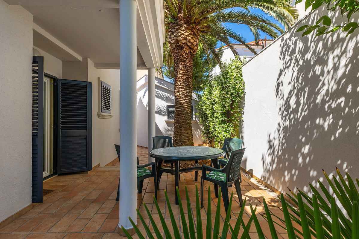 Una terrazza esterna con un tavolo rotondo e sedie, una palma e un muro bianco.