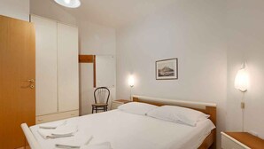Una habitación de hotel con cama, una silla, armario y mesita de noche.