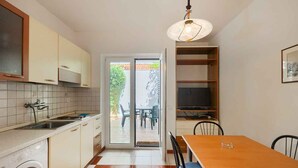 Cocina compacta con lavadora integrada, zona de comedor con mesa y sillas, y puerta corrediza de vidrio que da a un patio exterior.