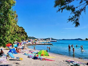 Ein Strand mit Zelten, Liegestühlen und badenden Personen.