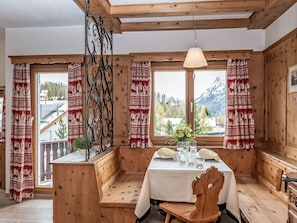 A wooden interior with a table set for dining, large windows with curtains, and a view of mountains.