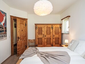 A bedroom with a bed, a wooden wardrobe, a chair, a lamp, and a poster on the wall.