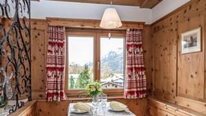 A wooden interior with a dining table set for two, a window with curtains, and a framed picture on the wall. - Chesa Minchületta by Interhome (Silvaplana-Surlej)