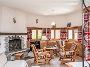 A cozy living room with a fireplace, wooden furniture, and patterned curtains.