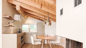 Una cocina moderna con vigas de madera, armarios blancos y una zona de comedor con una mesa redonda y sillas.