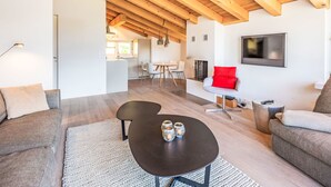 Una sala de estar moderna con techo de madera, una mesa de centro negra, un sofá gris y una butaca roja.