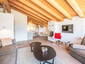 A modern living room with a wooden ceiling, a black coffee table, a grey sofa, and a red accent chair. - Cocoon-Laax by Interhome (Laax)