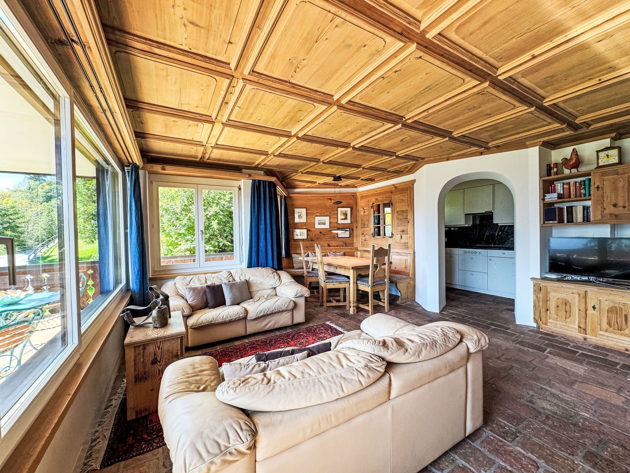 A cozy living room with a wooden ceiling, a dining area, and a kitchen with wooden cabinets.
