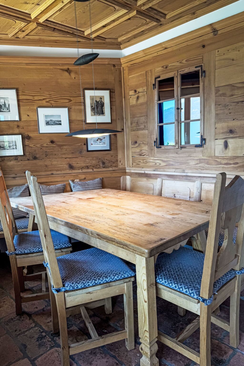 A wooden dining area with a large table and chairs, framed pictures on the wall, and a window with a view.