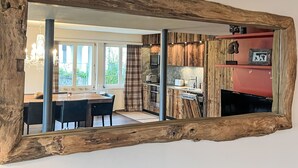 Una cocina moderna con detalles de madera, una zona de comedor con mesa y sillas, y un espejo grande con marco rústico.